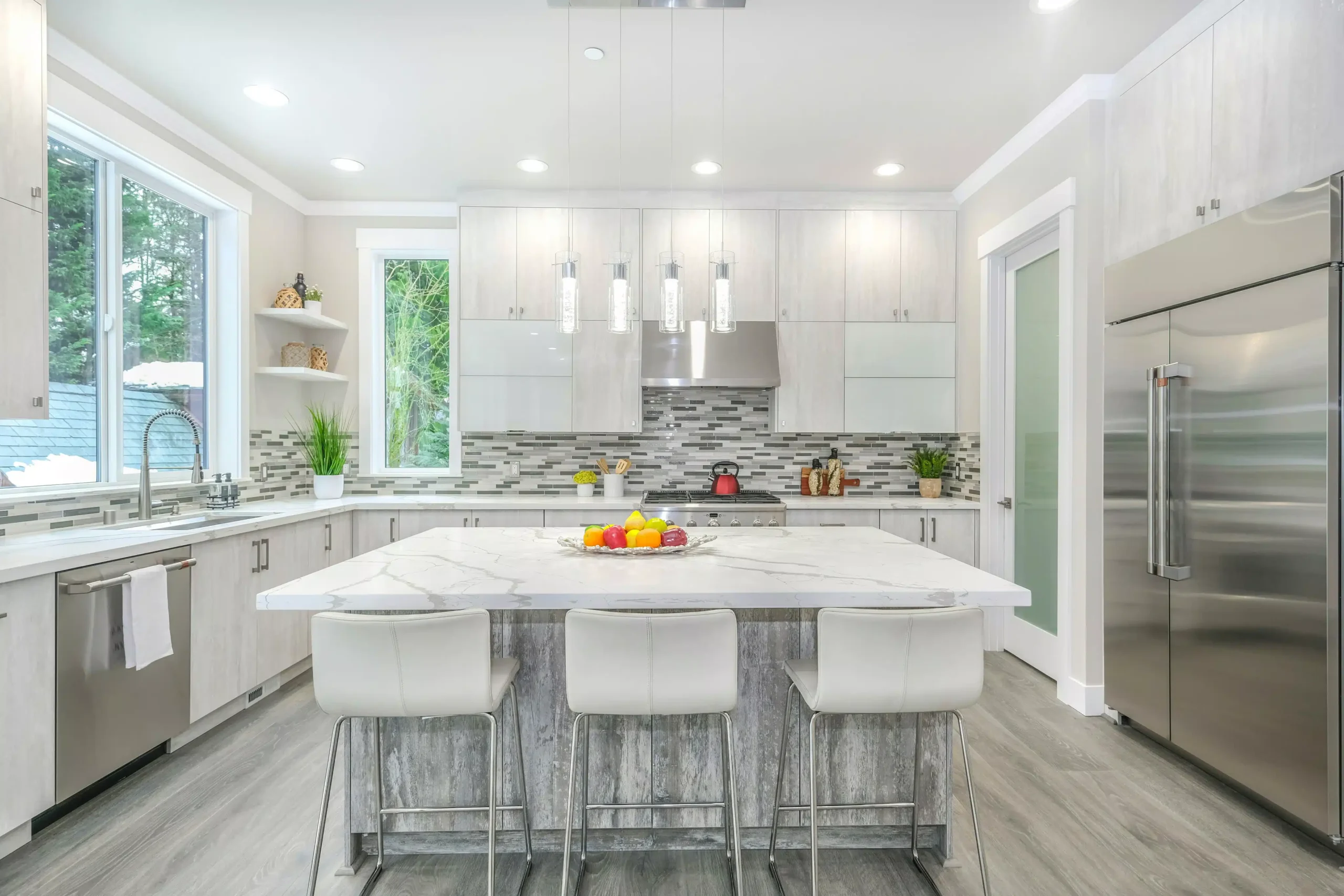 Modern kitchen with a marble island, white cabinets, stainless steel appliances, and pendant lights.